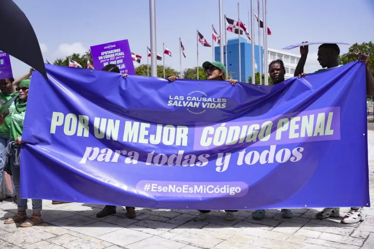 demonstrators hold up a purple banner with white letters reading better penal code for all